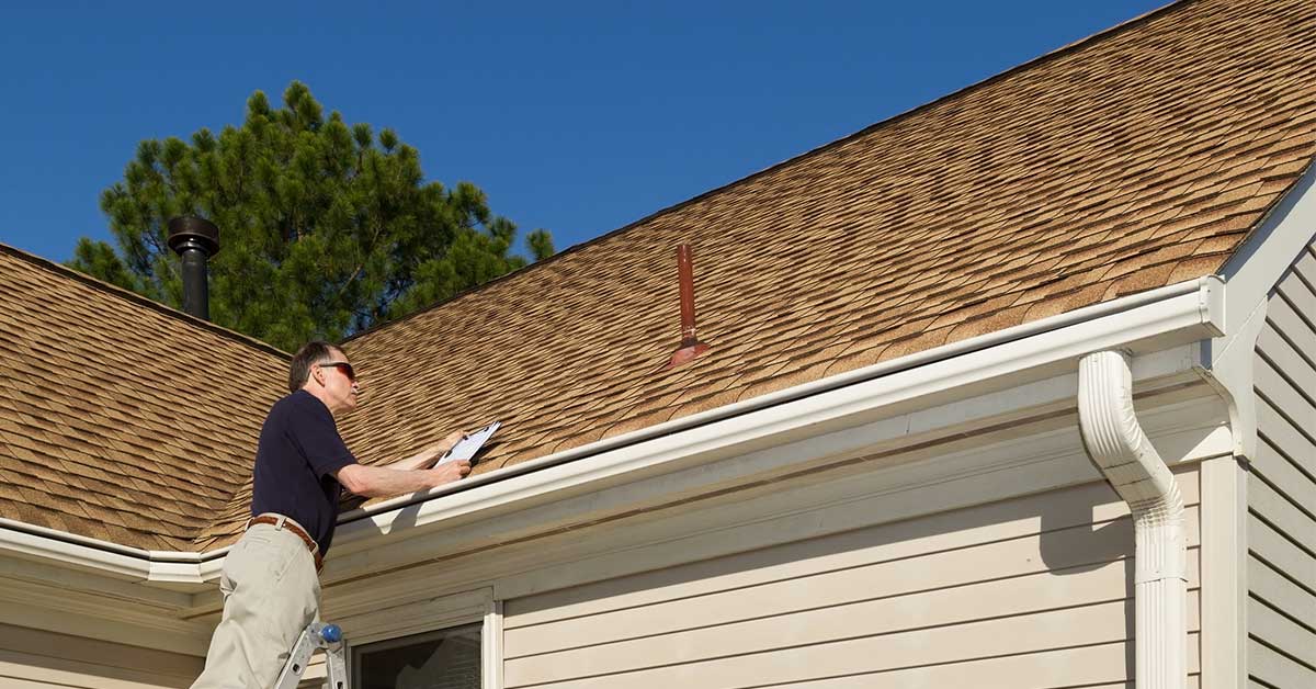 Man on ladder inspecting asphalt roof